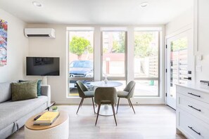 A modern living room with a sofa, a coffee table, and a TV. There is a dining area with a table and chairs, and a kitchen area with cabinets and a refrigerator. - Prime location w/ Private Parking & Rooftop Patio (Seattle)
