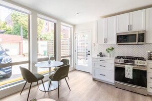 A modern kitchen with white cabinets, a gas stove, a microwave, and a dining area with a round table and chairs. - Prime location w/ Private Parking & Rooftop Patio (Seattle)