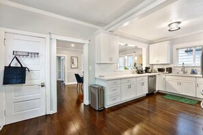 A modern kitchen with white cabinetry, a stainless steel refrigerator, and a microwave. - Remodeled Craftsman in Central District w/ Parking (Seattle)