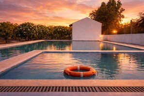 A swimming pool with a lifebuoy, surrounded by trees and a building. - Vanray Farm And Resort (Talala)