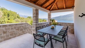 A covered outdoor dining area with a stone wall, wooden ceiling, and a view of a lake and mountains. - Luxury Villa Blue Dream (Đenovići)