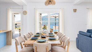 A dining area with a table set for six, large windows, and a view of the sea. - Luxury Villa Blue Dream (Đenovići)