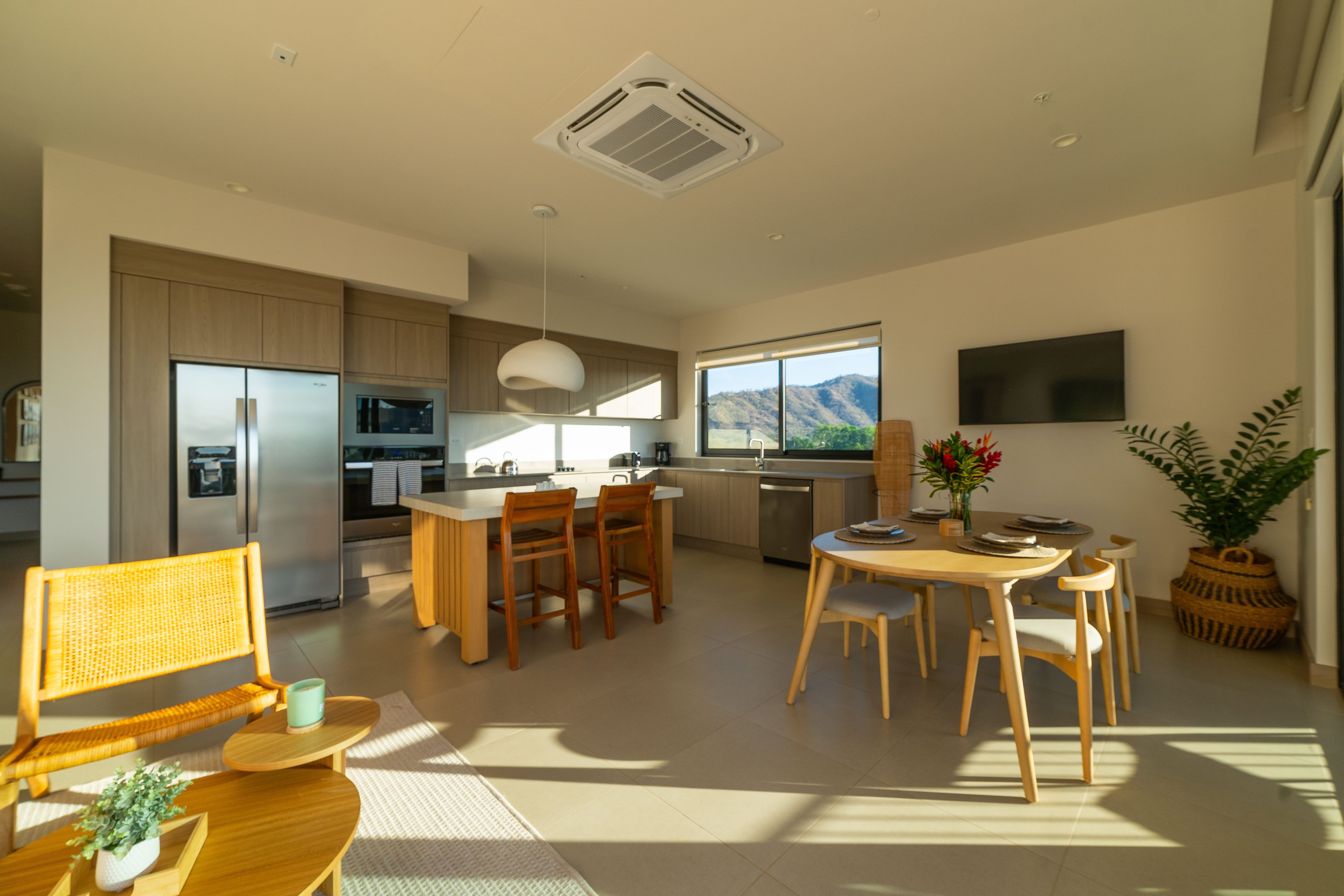 A modern kitchen with built-in appliances, a dining area with wooden furniture, and a large window offering a view of the outdoors.