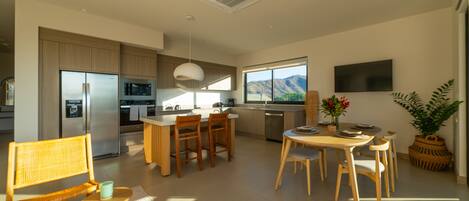 A modern kitchen with built-in appliances, a dining area with wooden furniture, and a large window offering a view of the outdoors.