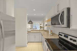 Una cocina moderna con armarios blancos, un refrigerador de acero inoxidable, un horno empotrado y un microondas.