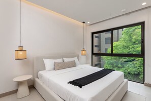A modern bedroom with a large bed, two bedside lamps, a small side table, and a large window with a view of greenery.