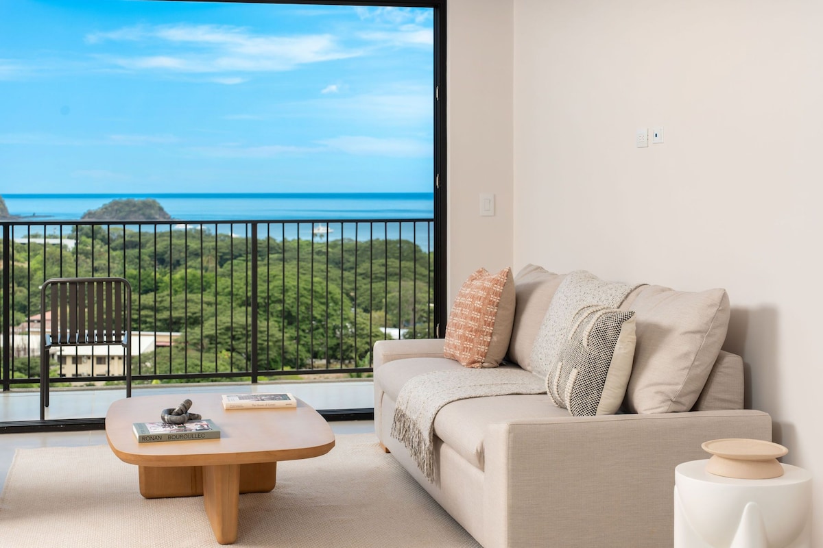 A living room with a sofa, a coffee table, and a view of the ocean.