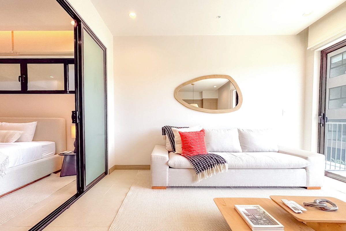 A modern hotel room with a bed, a sofa, a coffee table, and a large mirror.