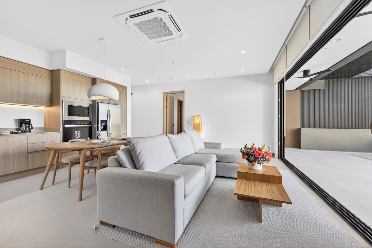 A modern living room with a sofa, a dining table, and a kitchen area with appliances.