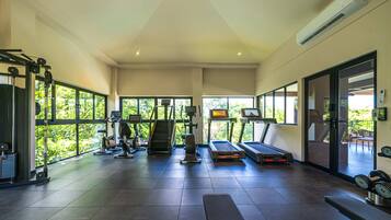 A spacious gym with various exercise equipment, large windows, and a view of greenery outside.