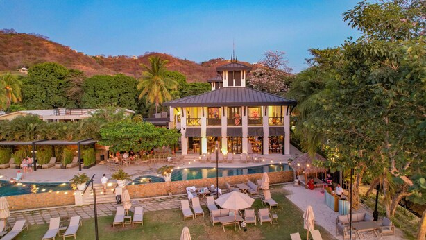 A resort with a pool, lounge chairs, and a building with a tower. - Pacifico Rentals (Sardinal)