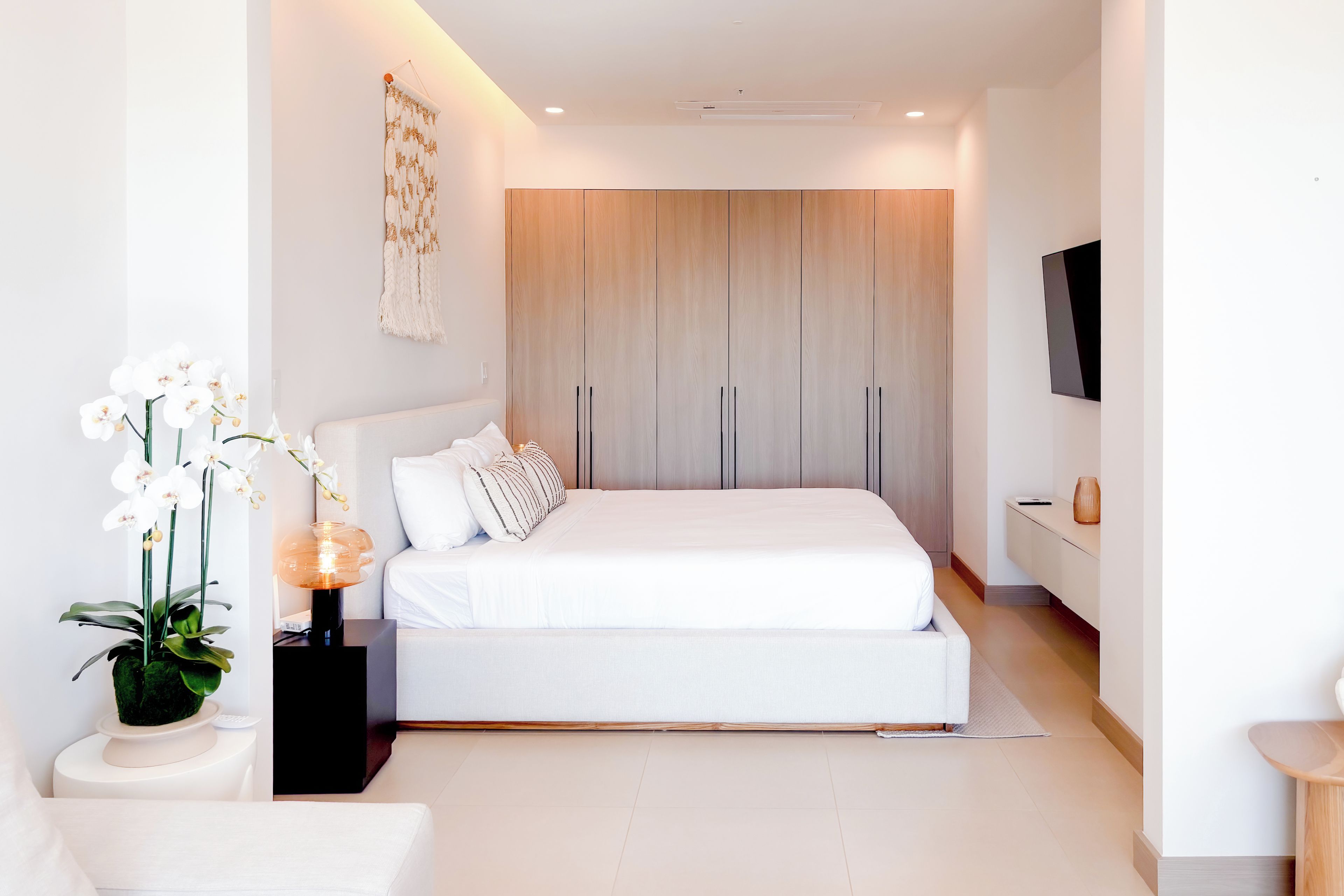 Un dormitorio moderno con una cama grande, una mesita de noche con lámpara y un televisor montado en la pared.