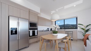 A modern kitchen with a built-in refrigerator, oven, and microwave. There's a dining table with chairs and a potted plant. - Pacifico Rentals (Sardinal)