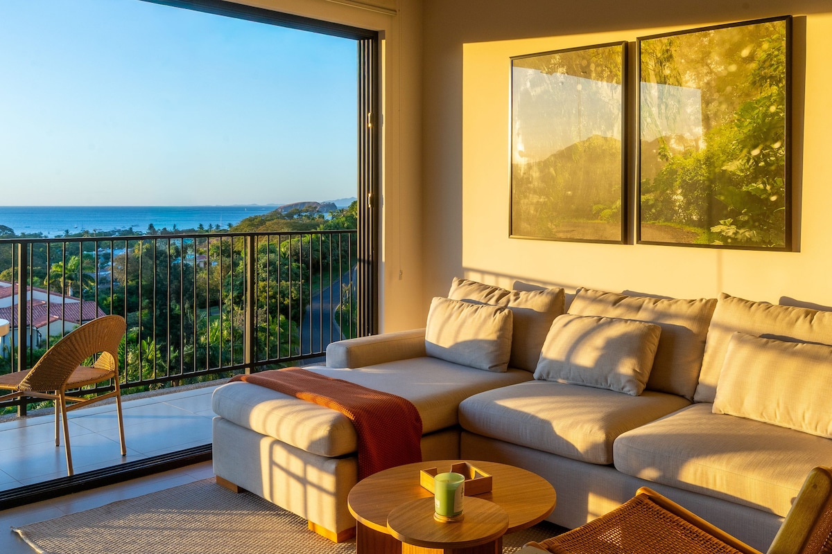 A living room with a sofa, a coffee table, and a view of the sea.
