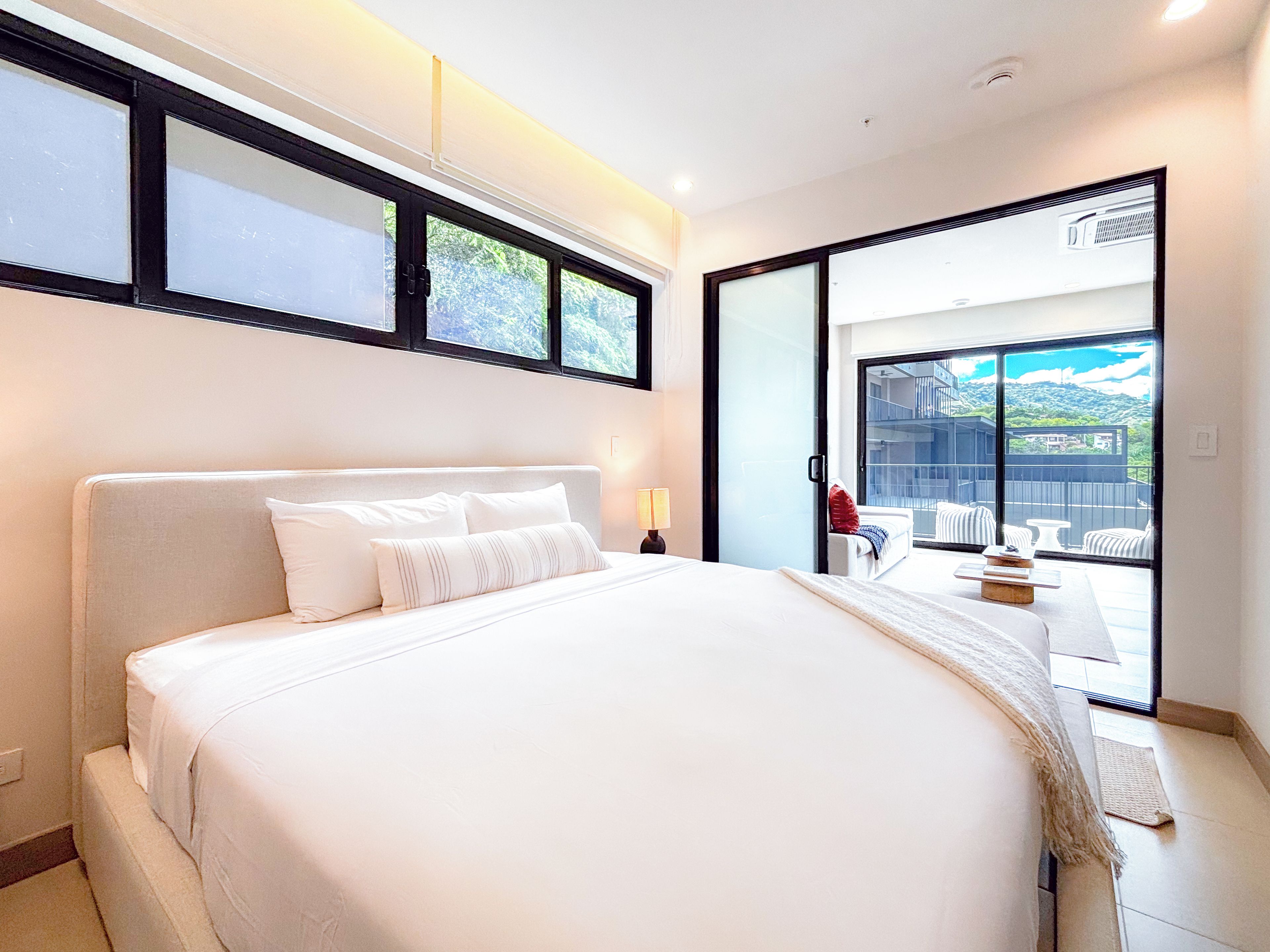 Quarto de hotel com cama grande, vista para o exterior e varanda com assentos.
