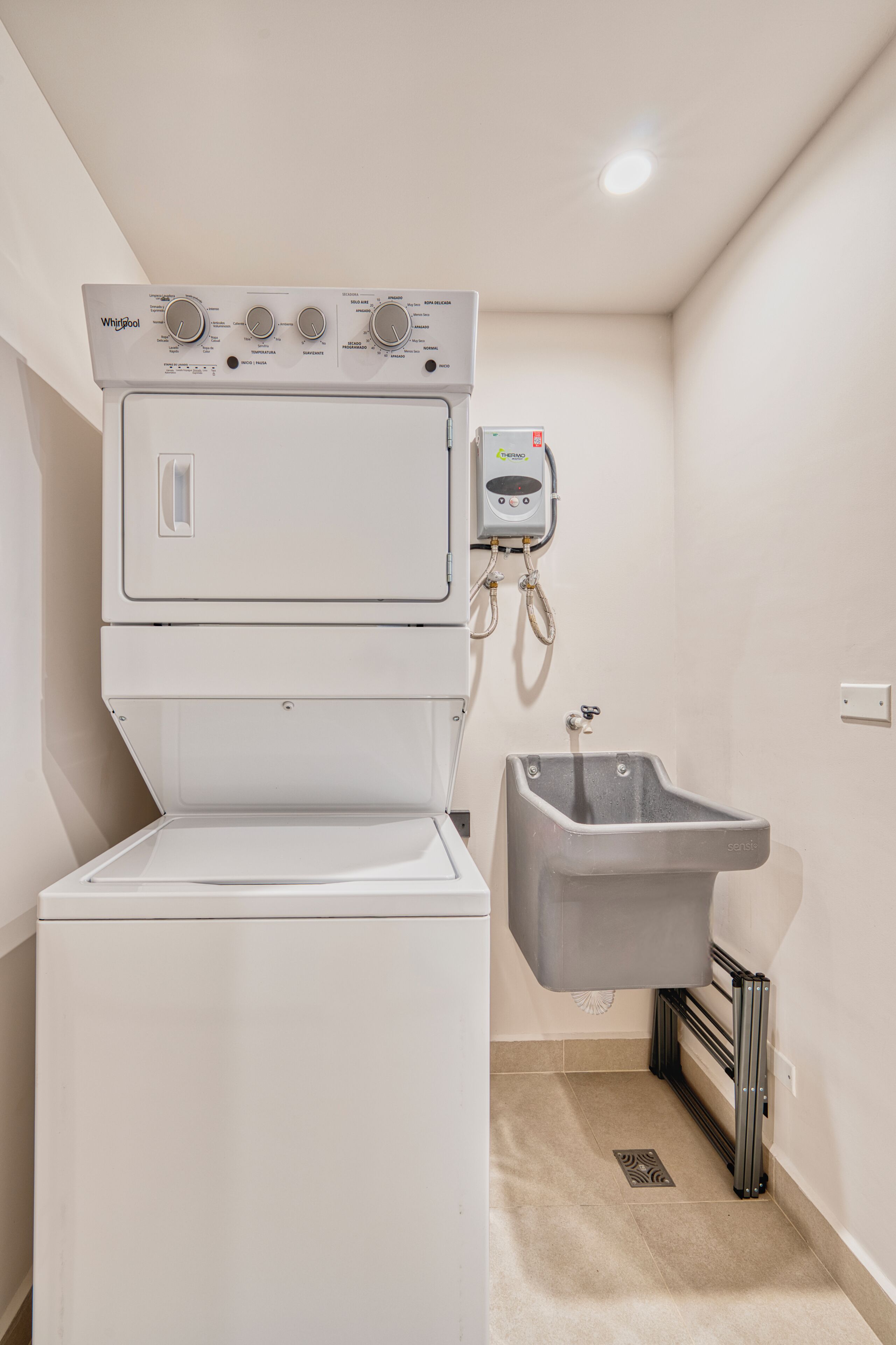A compact laundry room with a stacked washer and dryer, a built-in sink, and a visible water heater.