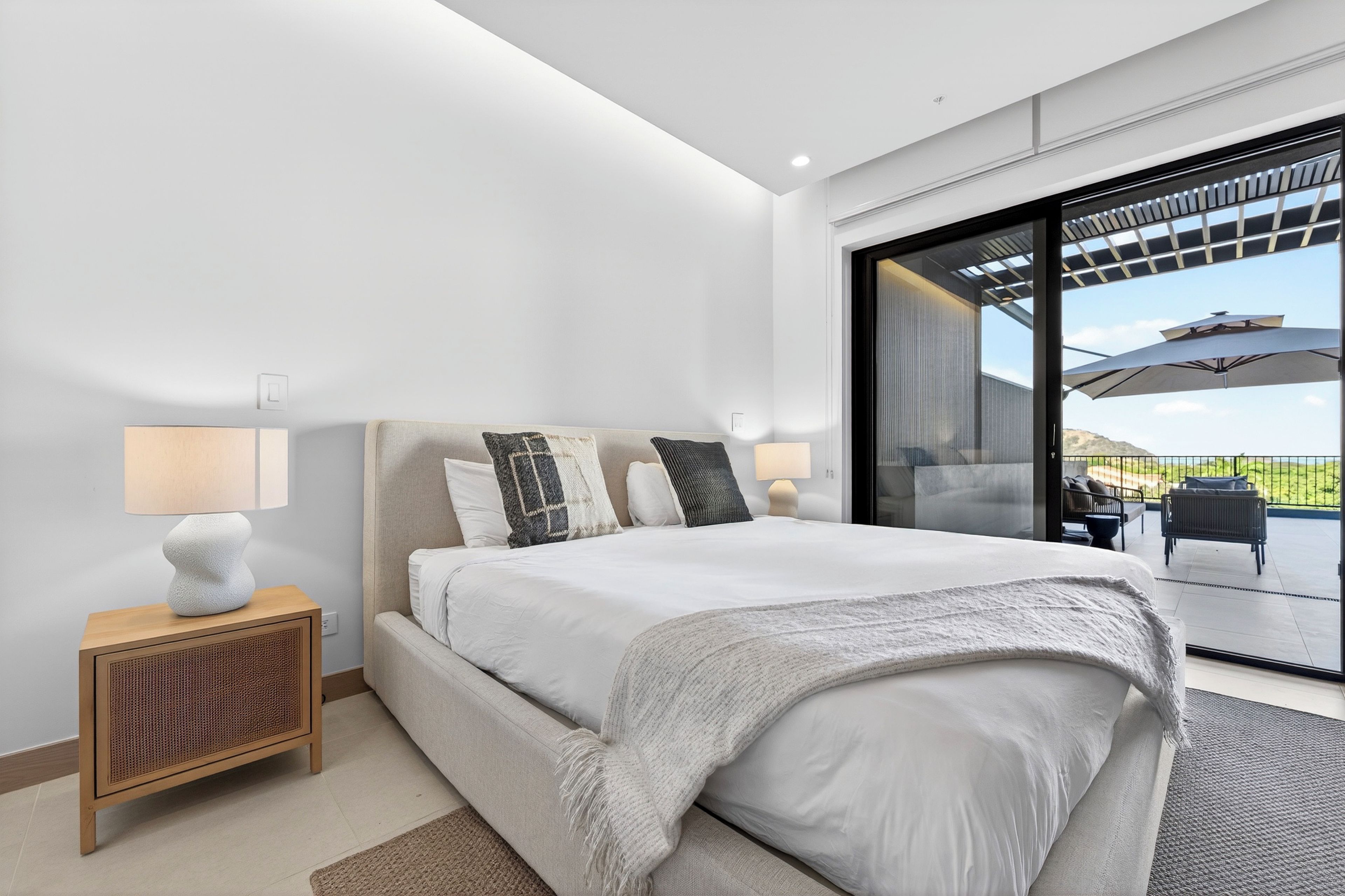 Een moderne slaapkamer met een groot bed, een nachtkastje, een lamp en uitzicht door een glazen deur op een terras.