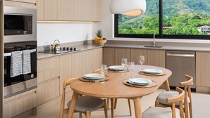 A modern kitchen with wooden cabinets, a stainless steel oven, and a dining area with a wooden table and chairs. - Pacifico Rentals (Sardinal)