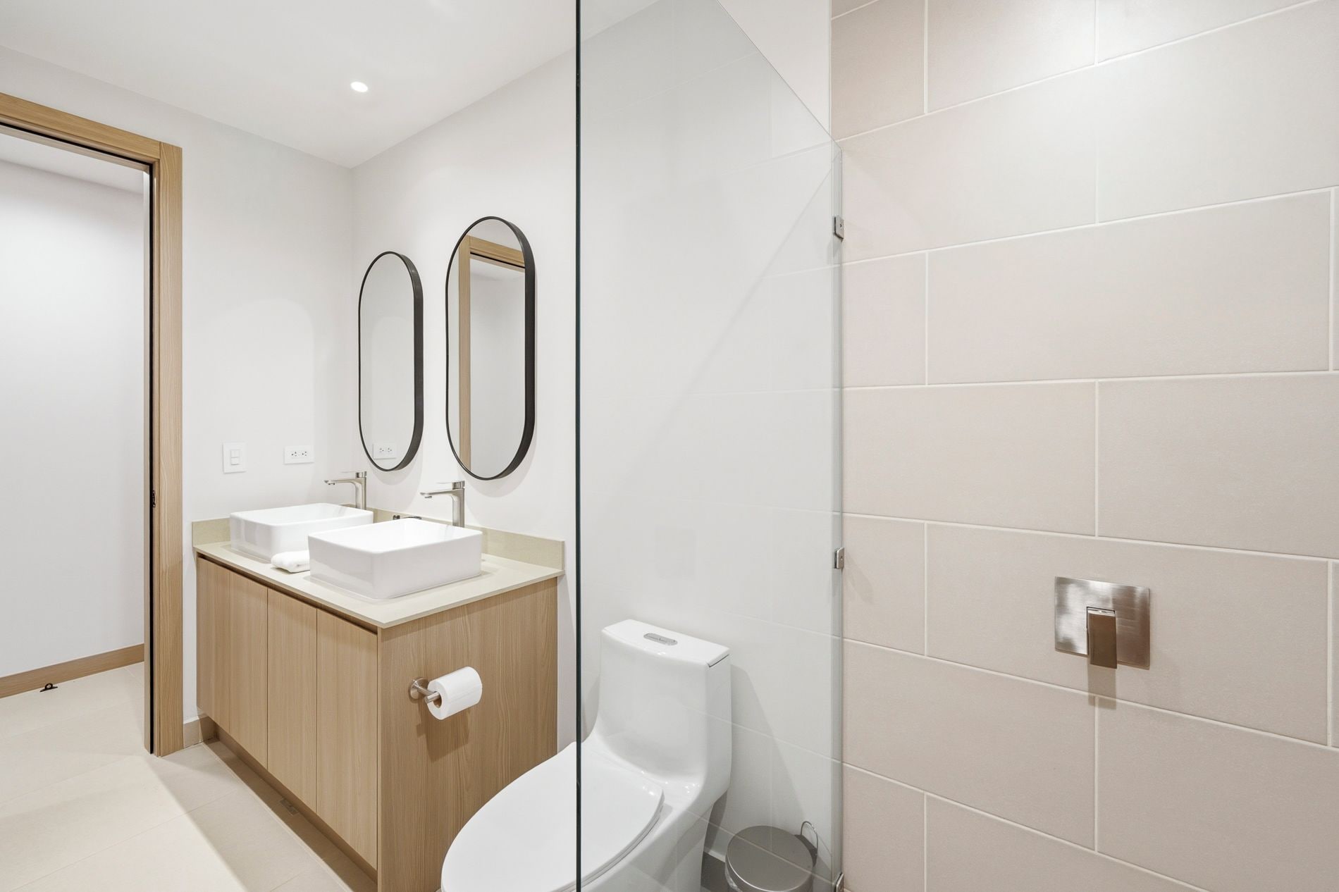 A modern bathroom with a wooden vanity, two sinks, a toilet, and a shower area.