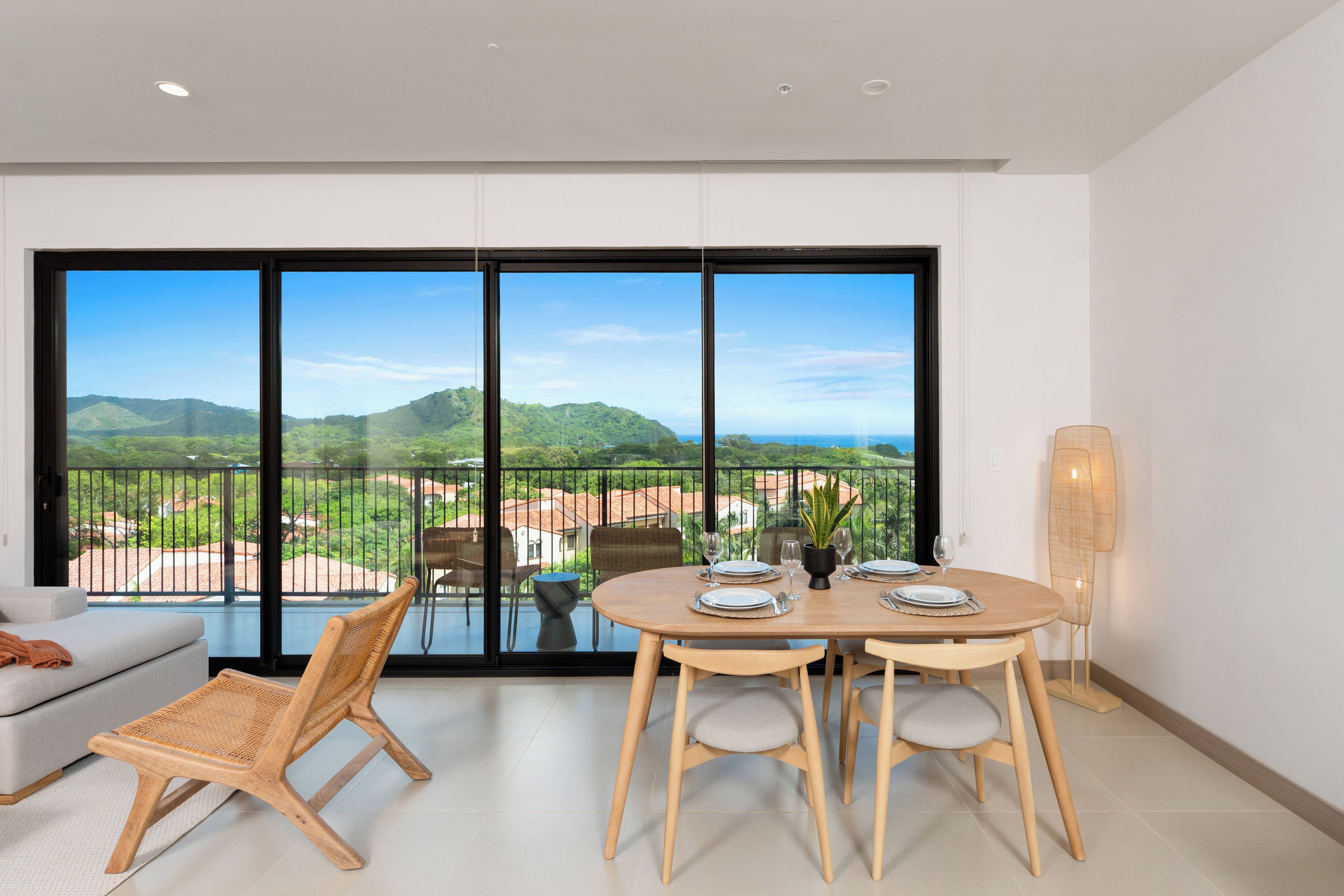 Una habitación moderna con un amplio ventanal corredero que da a un balcón con vistas panorámicas de colinas verdes y un cielo despejado.