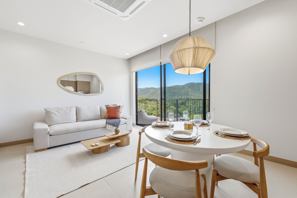 A modern dining area with a round table, chairs, and a view of a mountainous landscape through large windows.