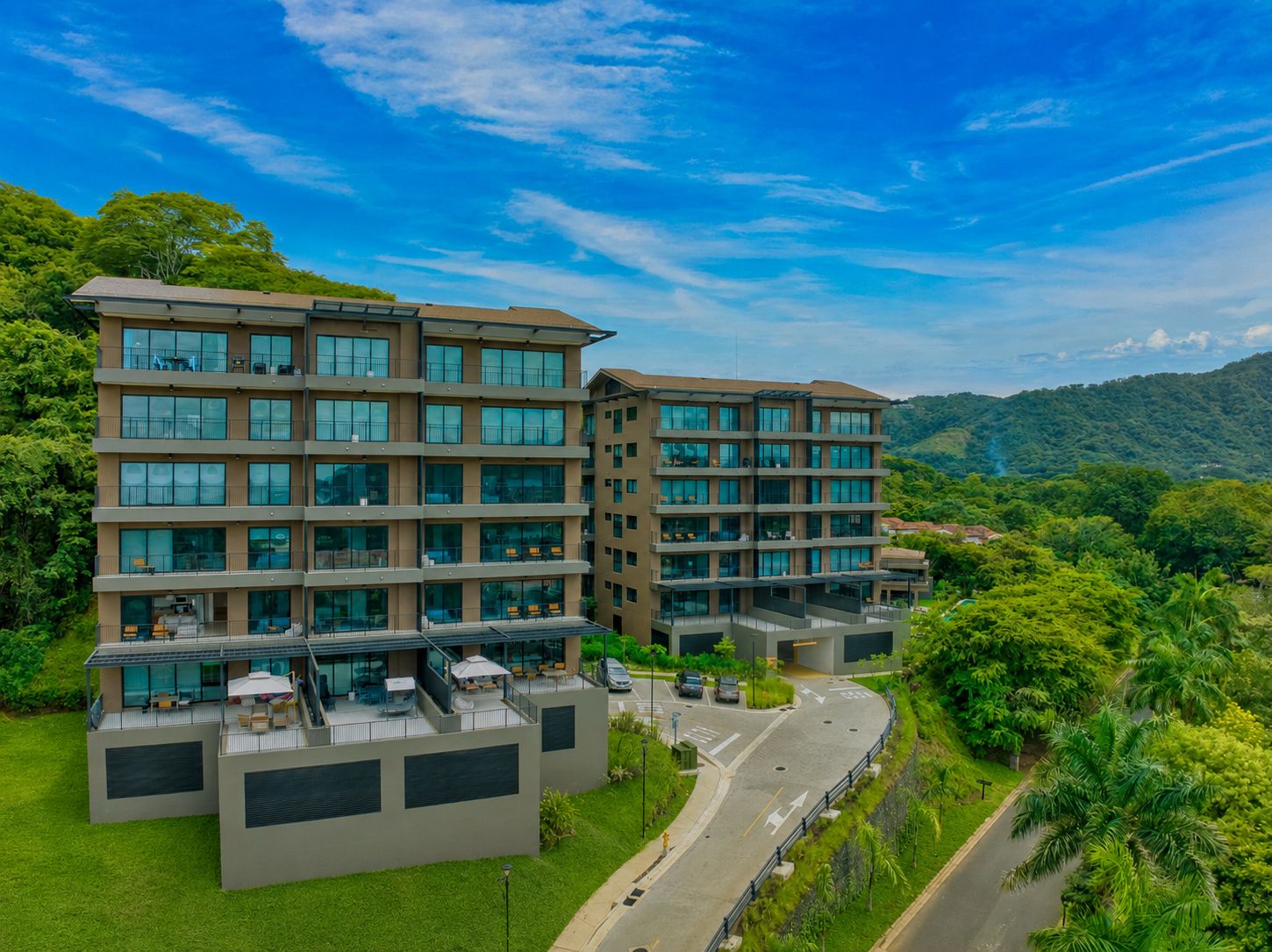 A multi-story hotel with a flat roof terrace and a view of the surrounding greenery.