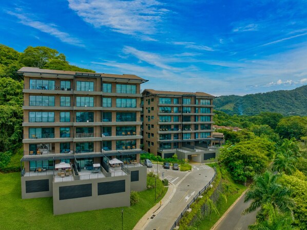 A multi-story hotel with a flat roof terrace and a view of the surrounding greenery.