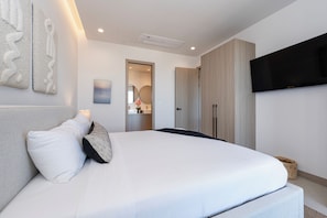 A modern bedroom with a large bed, a flat-screen TV mounted on the wall, and a minimalist decor style.