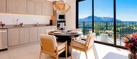 A modern kitchen with a dining area, large windows with a mountain view, and a dining table set for four.