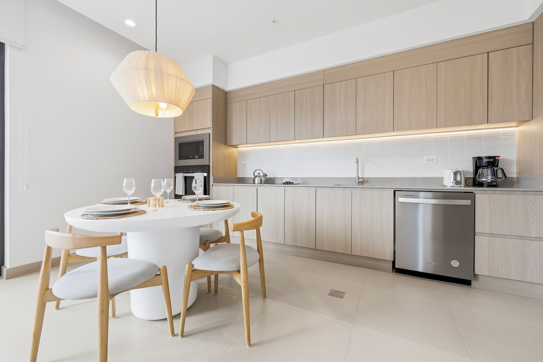 A modern kitchen with wooden cabinets, a stainless steel dishwasher, and a round dining table with chairs.