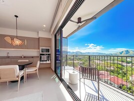 A modern kitchen with a dining area, a balcony with a view of mountains, and a ceiling fan.