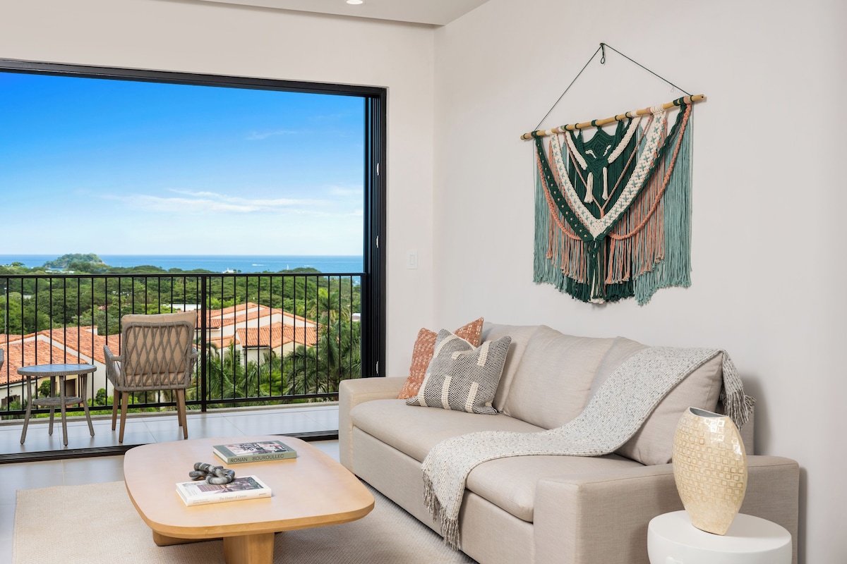 A living room with a sofa, a coffee table, and a view of the outdoors.
