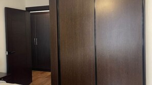 A room with a dark wooden wardrobe, a bed with a white mattress, and a wooden floor.