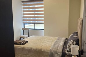 A bedroom with a bed, a chair, a window with blinds, and a bedside table with a lamp. - Two bedroom apartment in La Paz (La Paz)