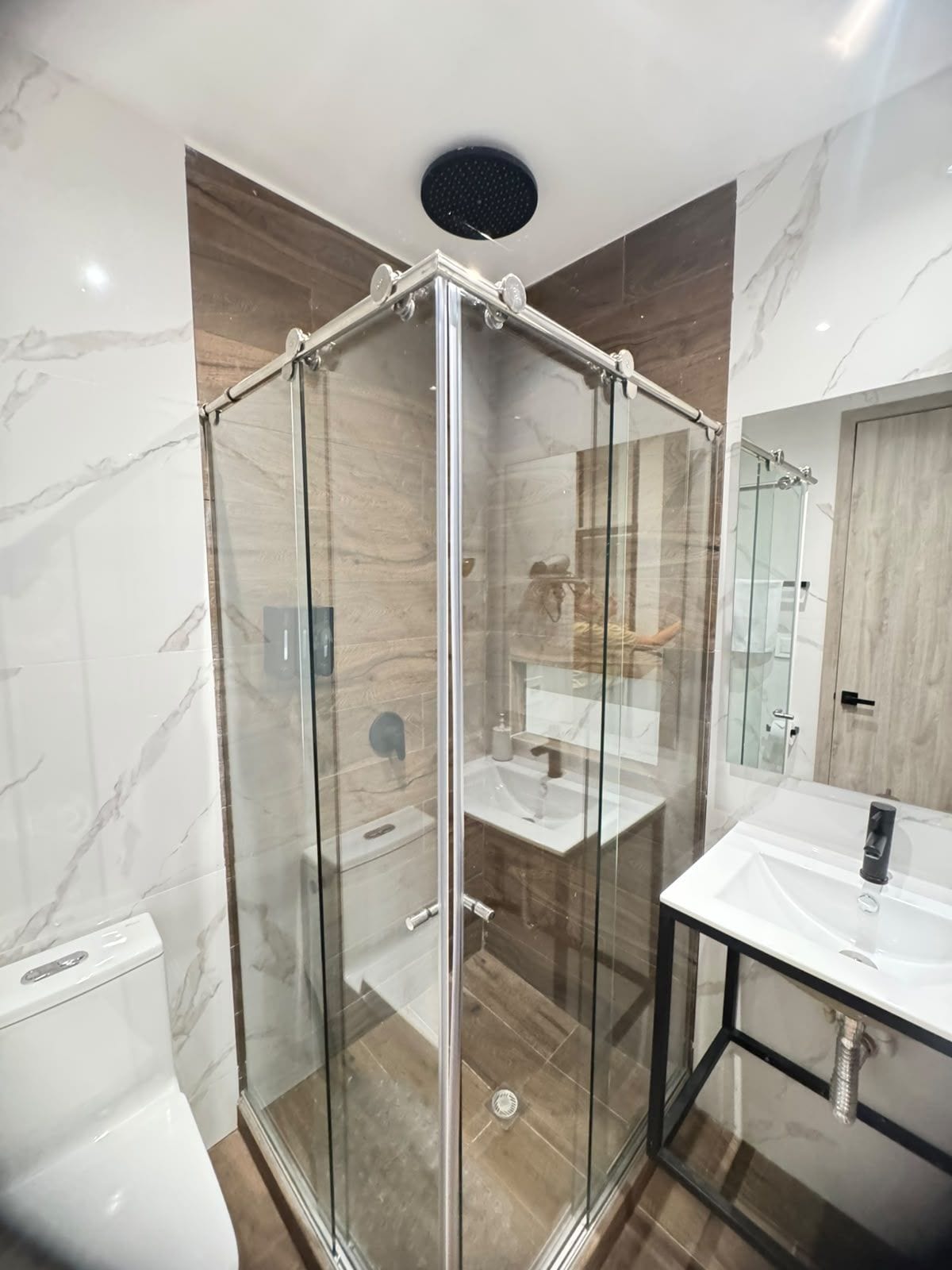 Une salle de bain moderne avec une douche à parois de verre, un lavabo blanc et un revêtement de sol en marbre.