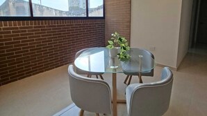 Een moderne eethoek met een glazen tafel, twee grijze stoelen en een potplant.
