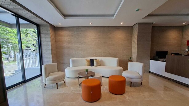 Een modern interieur met een witte zithoek, twee oranje poefs, een kleine ronde tafel en een receptiebalie.