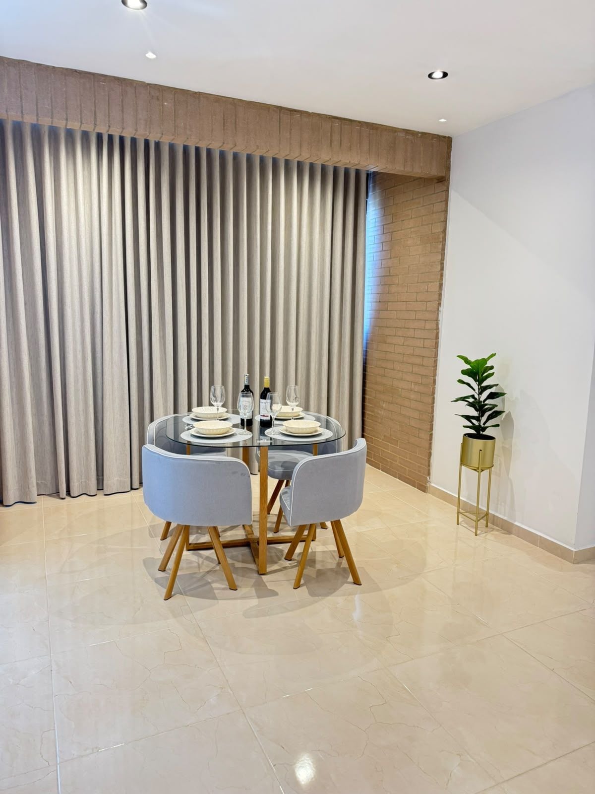 A dining area with a round glass table, grey chairs, and a potted plant.