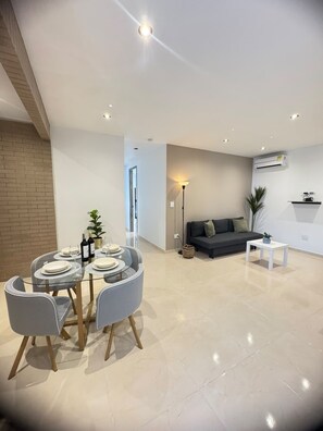A modern living room with a dining area, a sofa, a coffee table, and an air conditioning unit. - Apartamento Shanty tipo 2  (Barranquilla)