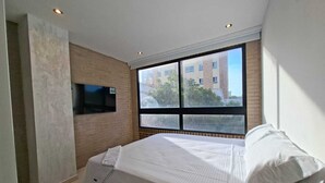 Een moderne hotelkamer met een groot bed, een flatscreen televisie aan de muur en een raam met uitzicht op gebouwen.