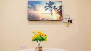 Une pièce avec une table ronde, un téléviseur fixé au mur qui diffuse une scène de coucher de soleil, et une prise de courant avec un multiprise.