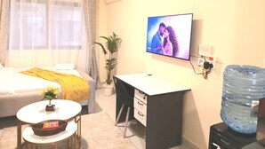 Une chambre d’hôtel équipée d’un lit, d’un bureau, d’une télévision, d’un distributeur d’eau et d’une plante.