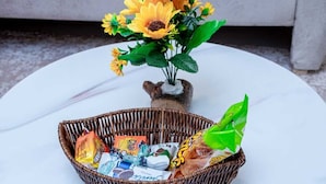 Une table ronde blanche sur laquelle se trouve un panier en osier contenant des en-cas et une petite plante en pot ornée de fleurs jaunes.