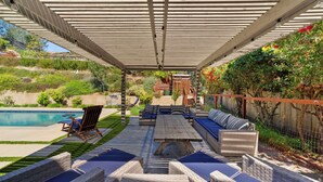Une terrasse couverte avec une piscine, des sièges d’extérieur et une vue sur le jardin arrière.