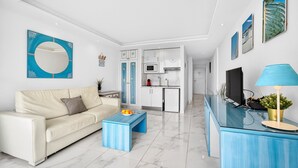 Ein modernes Wohnzimmer mit Sofa, Couchtisch und einer Küchenzeile im Hintergrund.