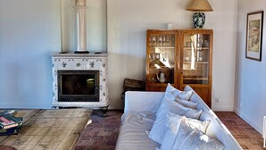 A rustic living room with exposed wooden beams, a white sofa, a wooden table, and a vintage stove. - Favorite house 1h15 Paris jacuzzi Fontainebleau countryside Moret Sur Loing (Lorrez-le-Bocage-Préaux)