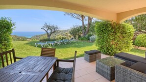 Eine Terrasse im Freien mit einem Holztisch und -stühlen, einer Rattan-Couch und Blick auf Meer und Hügel.