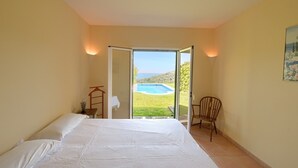 Ein Schlafzimmer mit Bett, einem Sessel, einer Tür, die zum Pool führt, und einem Bild an der Wand.