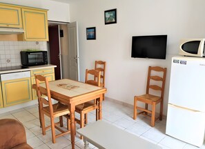 A kitchen with yellow cabinets, a microwave, a refrigerator, a dining table with chairs, and a television on the wall.