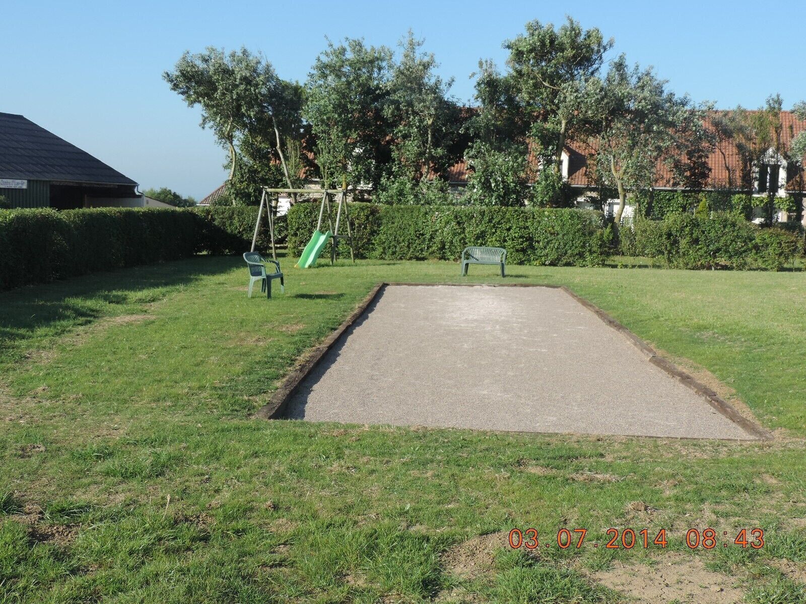 Um parque com área de lazer em concreto, bancos verdes e um escorrega.